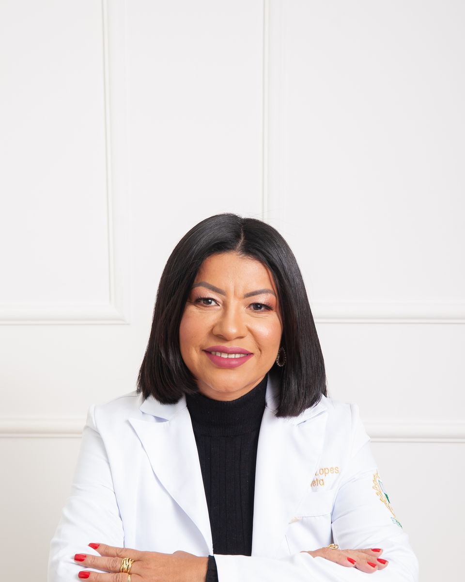 Dra. Neuma Lopes de jaleco, sorrindo, apoiada na mesa