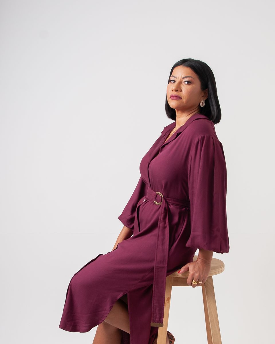 Dra. Neuma Lopes de vestido vinho, sentada em um banco alto