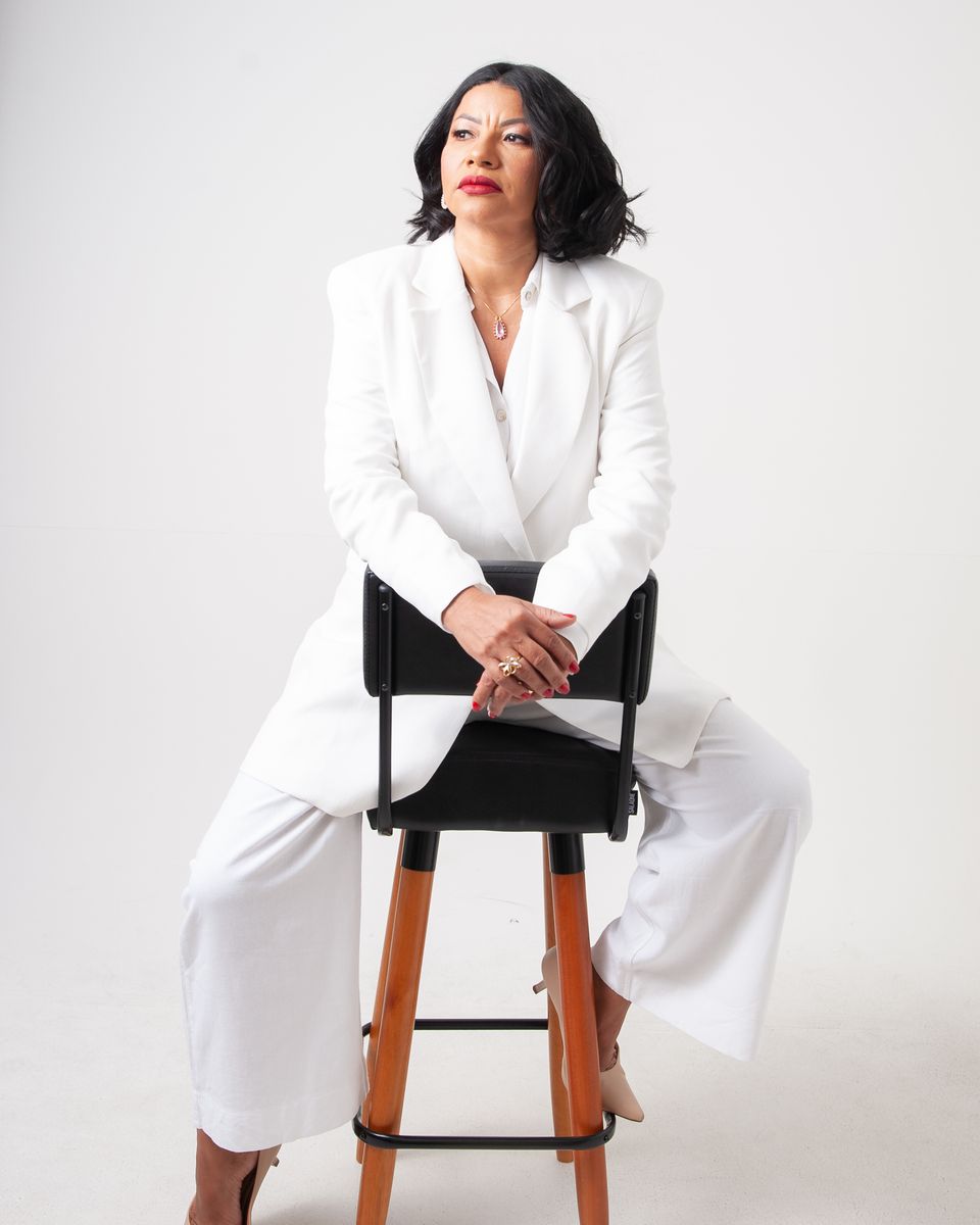 Dra. Neuma Lopes de terno branco, sentada em uma banqueta